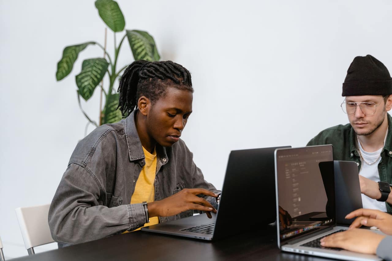 Two young adults working together on laptops in an office setting, focusing on tasks.